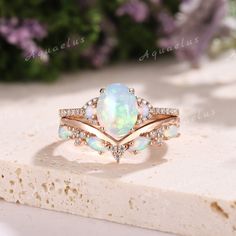 a white opal and diamond ring on top of a piece of stone with flowers in the background