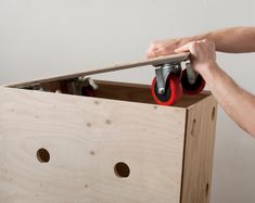 a person holding a pair of red wheels in a wooden box with holes on it