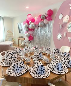 the table is set with black and white plates, silverware, and pink balloons