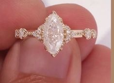 a close up of a person's hand holding an engagement ring with a pear shaped diamond