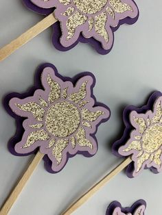 purple and gold decorated cookies on sticks with glitters in the shape of snowflakes