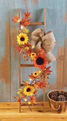 a wooden ladder with sunflowers and a bow on it next to a potted plant