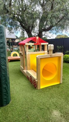 children's play area with wooden structure and red umbrellas on grass in front of large tree