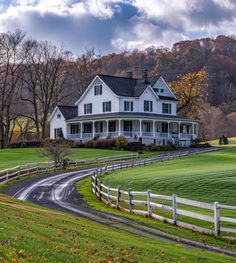 a large white house sitting in the middle of a lush green field next to a road