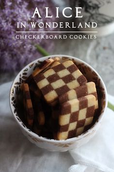 some brown and white squares are in a small bowl on a table next to purple flowers