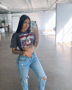 a woman taking a selfie with her cell phone in an empty room while wearing ripped jeans