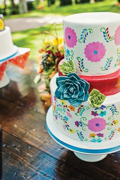 three tiered cake decorated with colorful flowers on a wooden table in front of other cakes