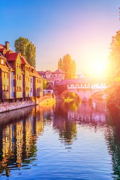 the sun is setting over some buildings on the side of a river with a bridge in the background