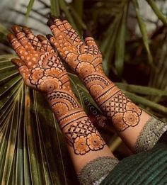 two hands with henna tattoos on them and palm leaves in the backgroun