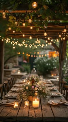 an outdoor dinner table with candles and greenery on the top, surrounded by lights