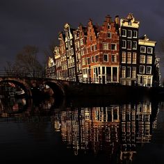 several buildings are reflected in the water on a dark night with a bridge crossing over it