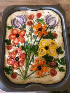 an uncooked pizza with tomatoes, onions and peppers on it in a pan