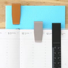 an open planner, ruler and pen on a wooden table with a blue wall behind it