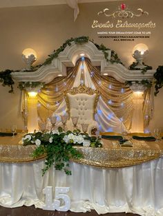 an elaborately decorated banquet table with flowers and greenery on the top, in front of a white backdrop