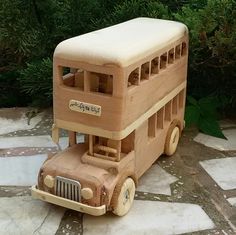 a wooden toy bus sitting on top of a stone floor next to green plants and bushes