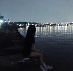 a woman sitting on the edge of a lake at night