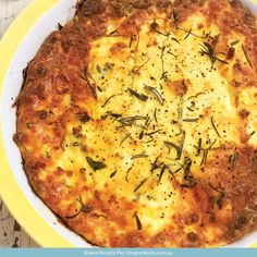 a pizza with cheese and herbs on it in a yellow dish sitting on a wooden table