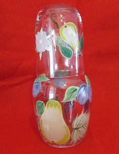 a glass vase with fruit and flowers painted on the bottom, sitting on a red background