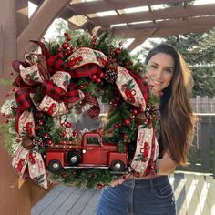 a woman holding up a christmas wreath with a red truck in the front and plaid bows on it