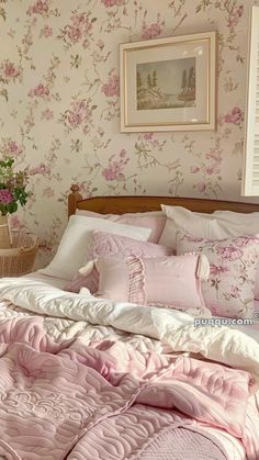 a bed with pink comforters and pillows in a room that has floral wallpaper on the walls