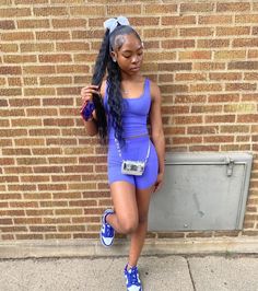 a woman with long hair standing in front of a brick wall wearing blue shorts and sneakers