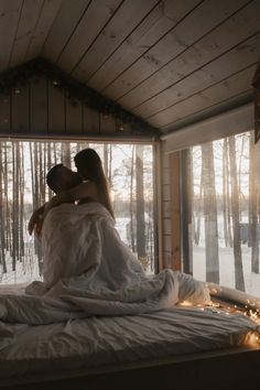 two people sitting on top of a bed covered in white sheets and blankets next to each other