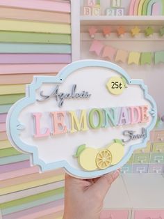 a person holding up a sign that says lemonade shop in front of a rainbow colored wall