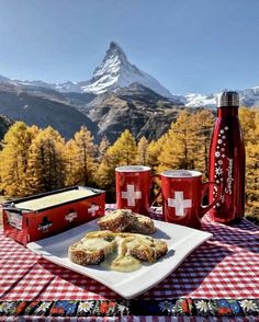 a plate of food and two cups on a table with mountains in the back ground