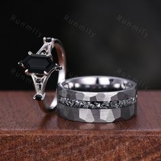 two wedding rings with black diamonds on them sitting on top of a wooden table next to each other