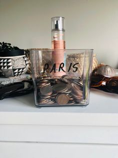 a clear container filled with coins on top of a white counter next to other items