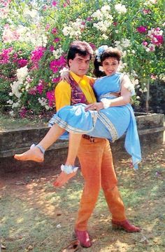 a man holding a woman in his arms while posing for a photo with flowers behind him