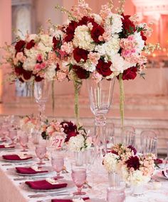 there are many tall vases filled with flowers on the long table set for an event