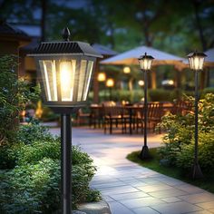 a lamp post in the middle of a walkway next to tables and chairs at night