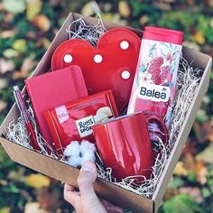 a person holding a box with various items in it that include soaps, toothpaste and heart shaped mugs