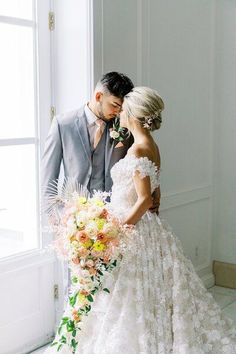 a bride and groom standing next to each other in front of a window with flowers