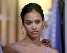 a young woman is holding on to her shirt and looking at the camera while wearing large hoop earrings