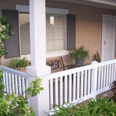 the front porch of a house with white railings and potted plants on it