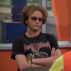 a man with his arms crossed sitting in front of an orange and blue wall wearing sunglasses