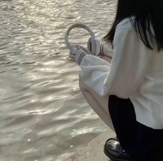 a woman sitting on the edge of a body of water holding a steering wheel