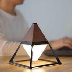 a person using a laptop on a wooden table with a lamp in front of them