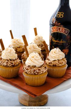 cupcakes with white frosting and cinnamon sticks on a plate next to a bottle of bailey's