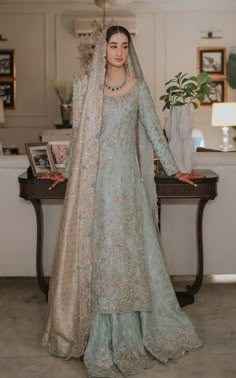 a woman standing in front of a table wearing a blue and gold dress with a veil on her head