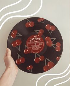 a hand holding an old record with red cherries on it and white lines in the background