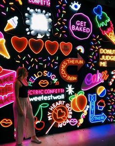 a woman standing in front of a wall covered with neon signs