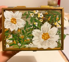 a hand holding a small box with flowers painted on it