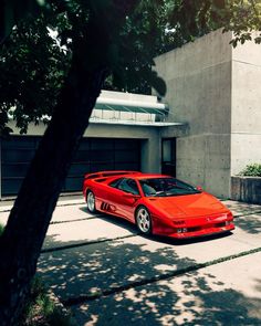 a red sports car parked in front of a building next to a tree and bushes