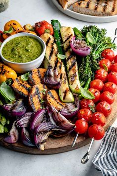 grilled chicken and vegetables on a wooden platter with pesto sauce in a bowl