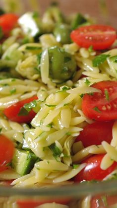 pasta salad with tomatoes, cucumbers and green beans in a glass bowl on a wooden table