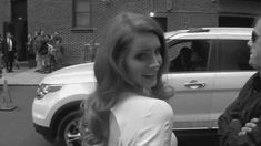 a woman standing next to a man in front of a white car on a city street