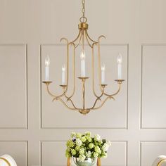 a chandelier hanging over a dining room table with chairs and flowers on it